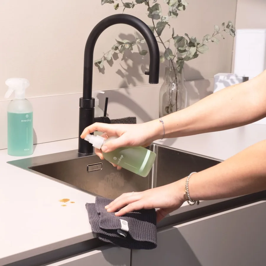 A cleaner wiping down a kitchen countertop with a spray bottle and cloth