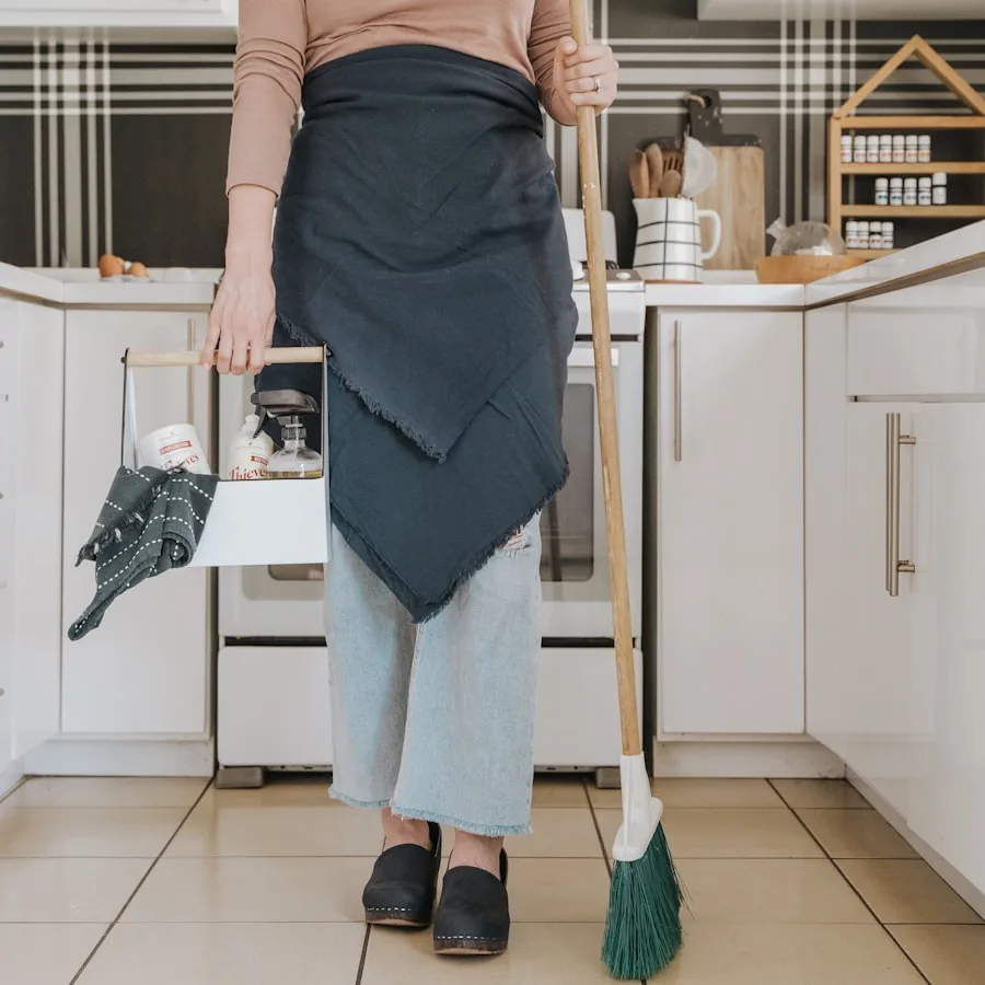 A cleaner in an apron carrying supplies through a home kitchen